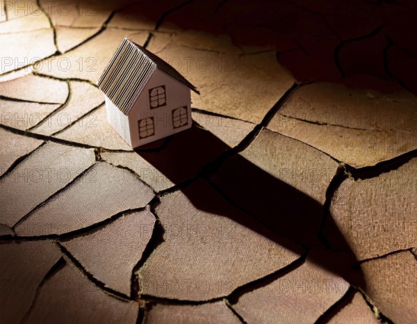 A cardboard miniature house placed on cracked, dry soil, illustrating drought, environmental impact, or harsh climatic conditions. An expression of vulnerability and adaptation amidst ecological challenges, AI generated