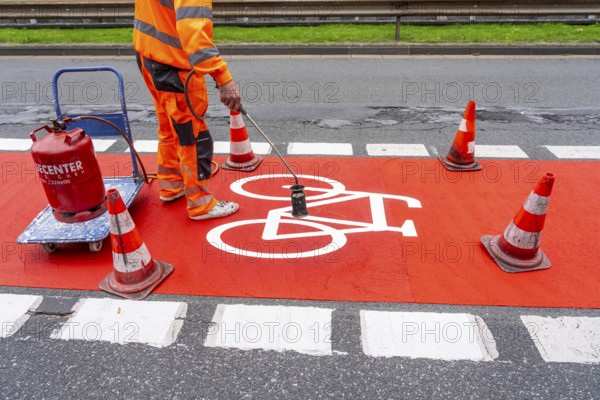 Application of red road surfacing on a cycle lane, inner-city road, so-called cold plastic surfacing, in the colour traffic red, RAL3020, the coloured marking is intended to attract more attention from motorists for cyclists, on cycle paths along roads and at junctions, roundabouts, Essen, North Rhine-Westphalia, Germany