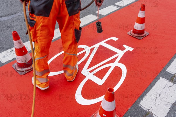 Application of red road surfacing on a cycle lane, inner-city road, so-called cold plastic surfacing, in the colour traffic red, RAL3020, the coloured marking is intended to attract more attention from motorists for cyclists, on cycle paths along roads and at junctions, roundabouts, Essen, North Rhine-Westphalia, Germany