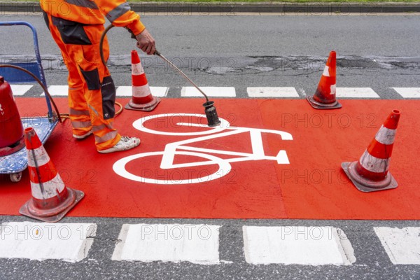 Application of red road surfacing on a cycle lane, inner-city road, so-called cold plastic surfacing, in the colour traffic red, RAL3020, the coloured marking is intended to attract more attention from motorists for cyclists, on cycle paths along roads and at junctions, roundabouts, Essen, North Rhine-Westphalia, Germany