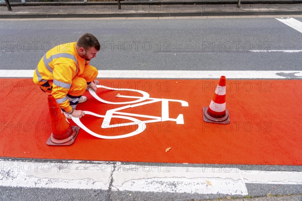 Application of red road surfacing on a cycle lane, inner-city road, so-called cold plastic surfacing, in the colour traffic red, RAL3020, the coloured marking is intended to attract more attention from motorists for cyclists, on cycle paths along roads and at junctions, roundabouts, Essen, North Rhine-Westphalia, Germany
