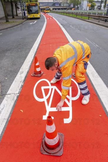 Application of red road surfacing on a cycle lane, inner-city road, so-called cold plastic surfacing, in the colour traffic red, RAL3020, the coloured marking is intended to attract more attention from motorists for cyclists, on cycle paths along roads and at junctions, roundabouts, Essen, North Rhine-Westphalia, Germany