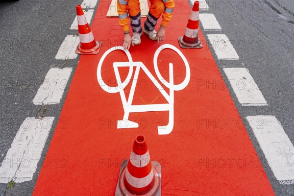 Application of red road surfacing on a cycle lane, inner-city road, so-called cold plastic surfacing, in the colour traffic red, RAL3020, the coloured marking is intended to attract more attention from motorists for cyclists, on cycle paths along roads and at junctions, roundabouts, Essen, North Rhine-Westphalia, Germany