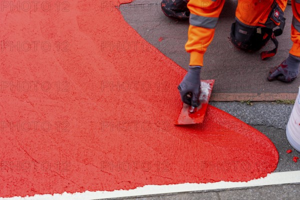 Application of red road surfacing on a cycle lane, inner-city road, so-called cold plastic surfacing, in the colour traffic red, RAL3020, the coloured marking is intended to attract more attention from motorists for cyclists, on cycle paths along roads and at junctions, roundabouts, Essen, North Rhine-Westphalia, Germany