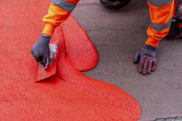 Application of red road surfacing on a cycle lane, inner-city road, so-called cold plastic surfacing, in the colour traffic red, RAL3020, the coloured marking is intended to attract more attention from motorists for cyclists, on cycle paths along roads and at junctions, roundabouts, Essen, North Rhine-Westphalia, Germany