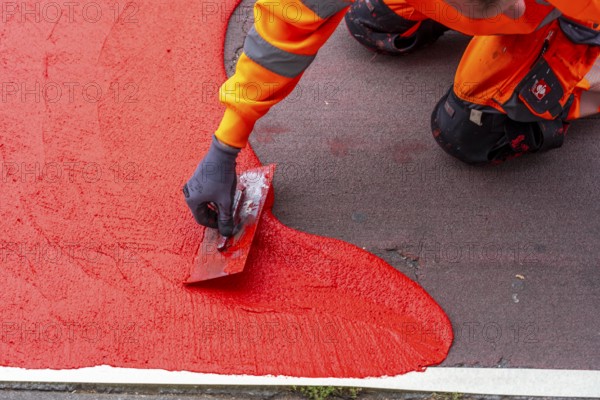 Application of red road surfacing on a cycle lane, inner-city road, so-called cold plastic surfacing, in the colour traffic red, RAL3020, the coloured marking is intended to attract more attention from motorists for cyclists, on cycle paths along roads and at junctions, roundabouts, Essen, North Rhine-Westphalia, Germany