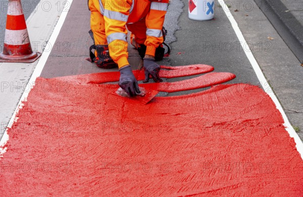 Application of red road surfacing on a cycle lane, inner-city road, so-called cold plastic surfacing, in the colour traffic red, RAL3020, the coloured marking is intended to attract more attention from motorists for cyclists, on cycle paths along roads and at junctions, roundabouts, Essen, North Rhine-Westphalia, Germany