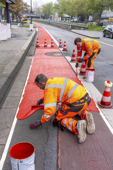 Application of red road surfacing on a cycle lane, inner-city road, so-called cold plastic surfacing, in the colour traffic red, RAL3020, the coloured marking is intended to attract more attention from motorists for cyclists, on cycle paths along roads and at junctions, roundabouts, Essen, North Rhine-Westphalia, Germany