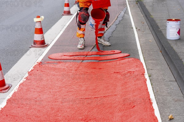Application of red road surfacing on a cycle lane, inner-city road, so-called cold plastic surfacing, in the colour traffic red, RAL3020, the coloured marking is intended to attract more attention from motorists for cyclists, on cycle paths along roads and at junctions, roundabouts, Essen, North Rhine-Westphalia, Germany