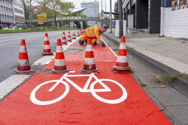 Application of red road surfacing on a cycle lane, inner-city road, so-called cold plastic surfacing, in the colour traffic red, RAL3020, the coloured marking is intended to attract more attention from motorists for cyclists, on cycle paths along roads and at junctions, roundabouts, Essen, North Rhine-Westphalia, Germany