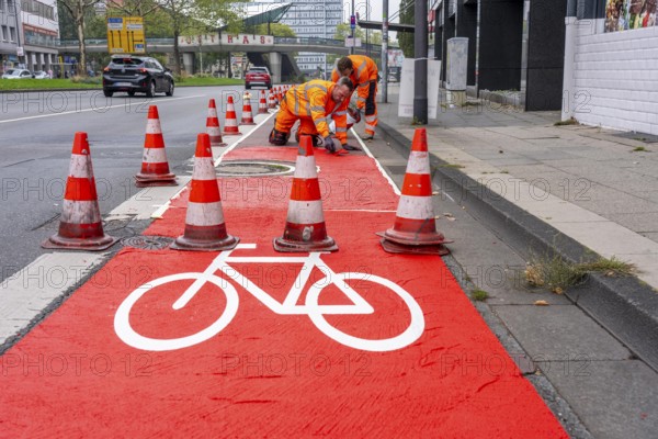 Application of red road surfacing on a cycle lane, inner-city road, so-called cold plastic surfacing, in the colour traffic red, RAL3020, the coloured marking is intended to attract more attention from motorists for cyclists, on cycle paths along roads and at junctions, roundabouts, Essen, North Rhine-Westphalia, Germany