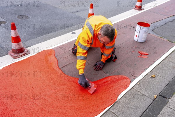 Application of red road surfacing on a cycle lane, inner-city road, so-called cold plastic surfacing, in the colour traffic red, RAL3020, the coloured marking is intended to attract more attention from motorists for cyclists, on cycle paths along roads and at junctions, roundabouts, Essen, North Rhine-Westphalia, Germany