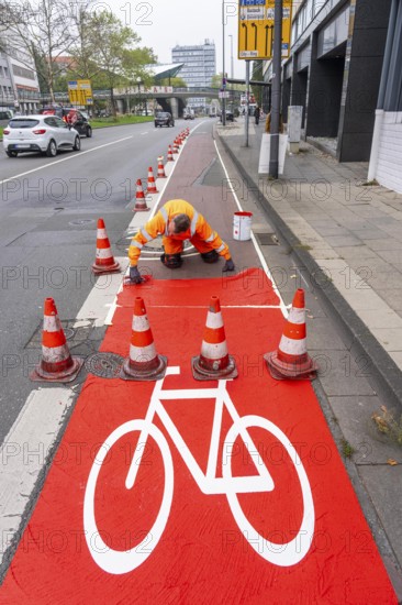 Application of red road surfacing on a cycle lane, inner-city road, so-called cold plastic surfacing, in the colour traffic red, RAL3020, the coloured marking is intended to attract more attention from motorists for cyclists, on cycle paths along roads and at junctions, roundabouts, Essen, North Rhine-Westphalia, Germany