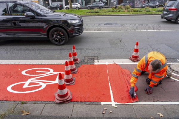 Application of red road surfacing on a cycle lane, inner-city road, so-called cold plastic surfacing, in the colour traffic red, RAL3020, the coloured marking is intended to attract more attention from motorists for cyclists, on cycle paths along roads and at junctions, roundabouts, Essen, North Rhine-Westphalia, Germany