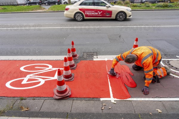 Application of red road surfacing on a cycle lane, inner-city road, so-called cold plastic surfacing, in the colour traffic red, RAL3020, the coloured marking is intended to attract more attention from motorists for cyclists, on cycle paths along roads and at junctions, roundabouts, Essen, North Rhine-Westphalia, Germany