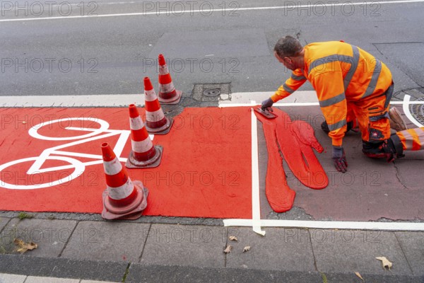 Application of red road surfacing on a cycle lane, inner-city road, so-called cold plastic surfacing, in the colour traffic red, RAL3020, the coloured marking is intended to attract more attention from motorists for cyclists, on cycle paths along roads and at junctions, roundabouts, Essen, North Rhine-Westphalia, Germany