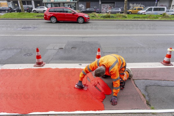 Application of red road surfacing on a cycle lane, inner-city road, so-called cold plastic surfacing, in the colour traffic red, RAL3020, the coloured marking is intended to attract more attention from motorists for cyclists, on cycle paths along roads and at junctions, roundabouts, Essen, North Rhine-Westphalia, Germany