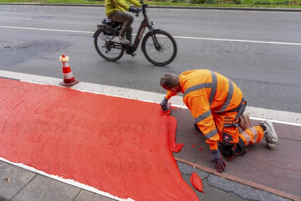 Application of red road surfacing on a cycle lane, inner-city road, so-called cold plastic surfacing, in the colour traffic red, RAL3020, the coloured marking is intended to attract more attention from motorists for cyclists, on cycle paths along roads and at junctions, roundabouts, Essen, North Rhine-Westphalia, Germany