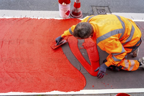 Application of red road surfacing on a cycle lane, inner-city road, so-called cold plastic surfacing, in the colour traffic red, RAL3020, the coloured marking is intended to attract more attention from motorists for cyclists, on cycle paths along roads and at junctions, roundabouts, Essen, North Rhine-Westphalia, Germany