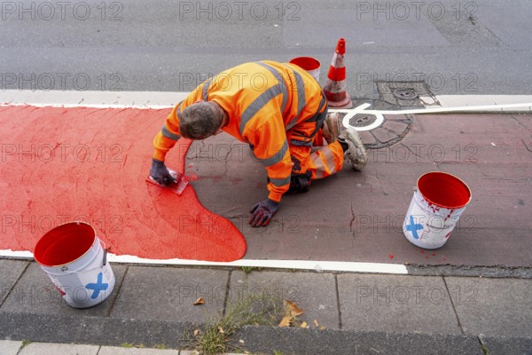 Application of red road surfacing on a cycle lane, inner-city road, so-called cold plastic surfacing, in the colour traffic red, RAL3020, the coloured marking is intended to attract more attention from motorists for cyclists, on cycle paths along roads and at junctions, roundabouts, Essen, North Rhine-Westphalia, Germany