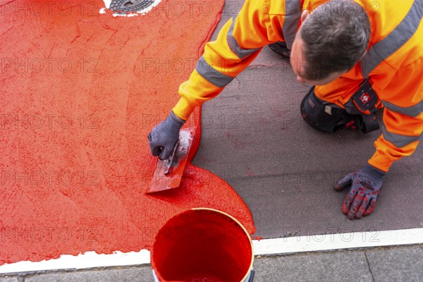 Application of red road surfacing on a cycle lane, inner-city road, so-called cold plastic surfacing, in the colour traffic red, RAL3020, the coloured marking is intended to attract more attention from motorists for cyclists, on cycle paths along roads and at junctions, roundabouts, Essen, North Rhine-Westphalia, Germany