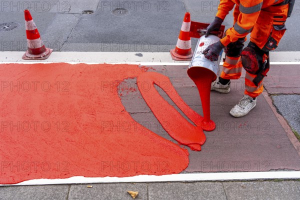 Application of red road surfacing on a cycle lane, inner-city road, so-called cold plastic surfacing, in the colour traffic red, RAL3020, the coloured marking is intended to attract more attention from motorists for cyclists, on cycle paths along roads and at junctions, roundabouts, Essen, North Rhine-Westphalia, Germany
