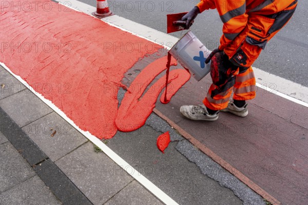 Application of red road surfacing on a cycle lane, inner-city road, so-called cold plastic surfacing, in the colour traffic red, RAL3020, the coloured marking is intended to attract more attention from motorists for cyclists, on cycle paths along roads and at junctions, roundabouts, Essen, North Rhine-Westphalia, Germany