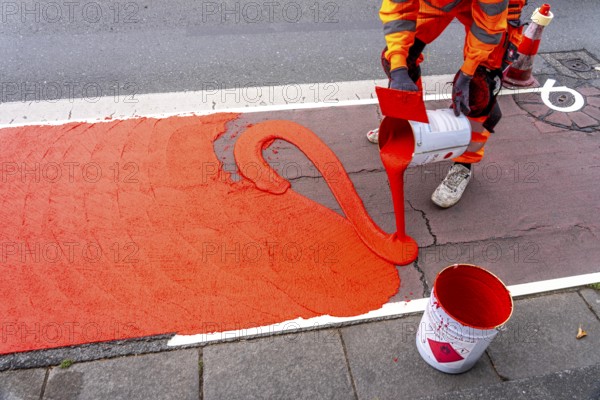 Application of red road surfacing on a cycle lane, inner-city road, so-called cold plastic surfacing, in the colour traffic red, RAL3020, the coloured marking is intended to attract more attention from motorists for cyclists, on cycle paths along roads and at junctions, roundabouts, Essen, North Rhine-Westphalia, Germany