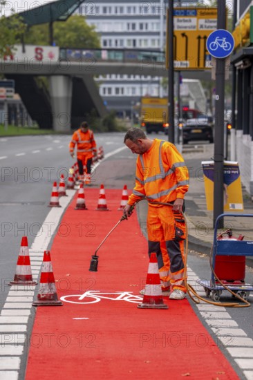 Application of red road surfacing on a cycle lane, inner-city road, so-called cold plastic surfacing, in the colour traffic red, RAL3020, the coloured marking is intended to attract more attention from motorists for cyclists, on cycle paths along roads and at junctions, roundabouts, Essen, North Rhine-Westphalia, Germany