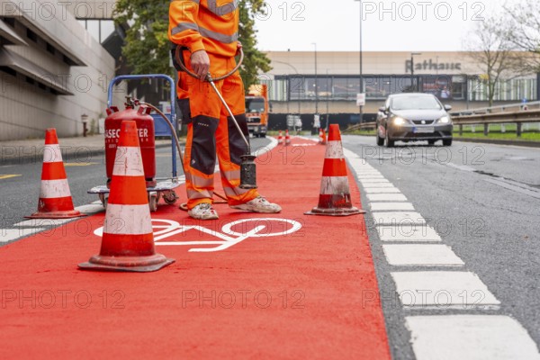 Application of red road surfacing on a cycle lane, inner-city road, so-called cold plastic surfacing, in the colour traffic red, RAL3020, the coloured marking is intended to attract more attention from motorists for cyclists, on cycle paths along roads and at junctions, roundabouts, Essen, North Rhine-Westphalia, Germany