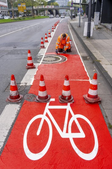Application of red road surfacing on a cycle lane, inner-city road, so-called cold plastic surfacing, in the colour traffic red, RAL3020, the coloured marking is intended to attract more attention from motorists for cyclists, on cycle paths along roads and at junctions, roundabouts, Essen, North Rhine-Westphalia, Germany