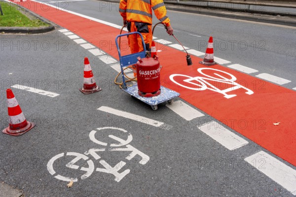 Application of red road surfacing on a cycle lane, inner-city road, so-called cold plastic surfacing, in the colour traffic red, RAL3020, the coloured marking is intended to attract more attention from motorists for cyclists, on cycle paths along roads and at junctions, roundabouts, Essen, North Rhine-Westphalia, Germany