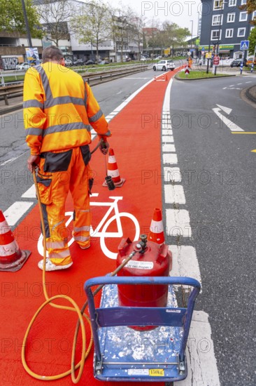 Application of red road surfacing on a cycle lane, inner-city road, so-called cold plastic surfacing, in the colour traffic red, RAL3020, the coloured marking is intended to attract more attention from motorists for cyclists, on cycle paths along roads and at junctions, roundabouts, Essen, North Rhine-Westphalia, Germany