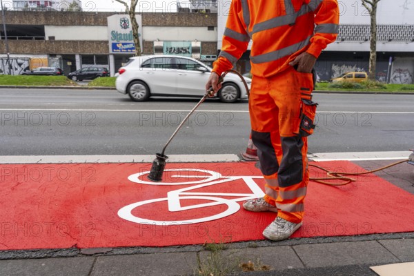 Application of red road surfacing on a cycle lane, inner-city road, so-called cold plastic surfacing, in the colour traffic red, RAL3020, the coloured marking is intended to attract more attention from motorists for cyclists, on cycle paths along roads and at junctions, roundabouts, Essen, North Rhine-Westphalia, Germany