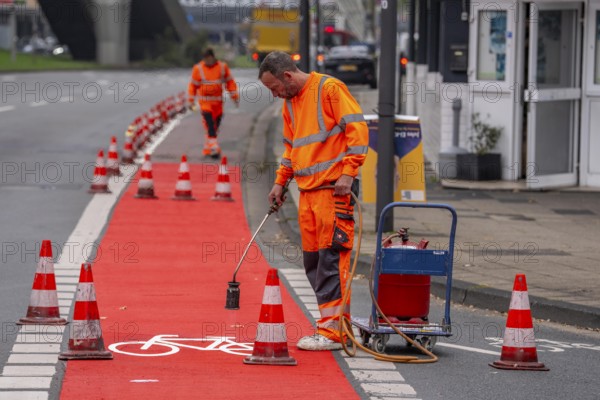 Application of red road surfacing on a cycle lane, inner-city road, so-called cold plastic surfacing, in the colour traffic red, RAL3020, the coloured marking is intended to attract more attention from motorists for cyclists, on cycle paths along roads and at junctions, roundabouts, Essen, North Rhine-Westphalia, Germany
