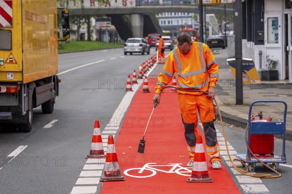 Application of red road surfacing on a cycle lane, inner-city road, so-called cold plastic surfacing, in the colour traffic red, RAL3020, the coloured marking is intended to attract more attention from motorists for cyclists, on cycle paths along roads and at junctions, roundabouts, Essen, North Rhine-Westphalia, Germany