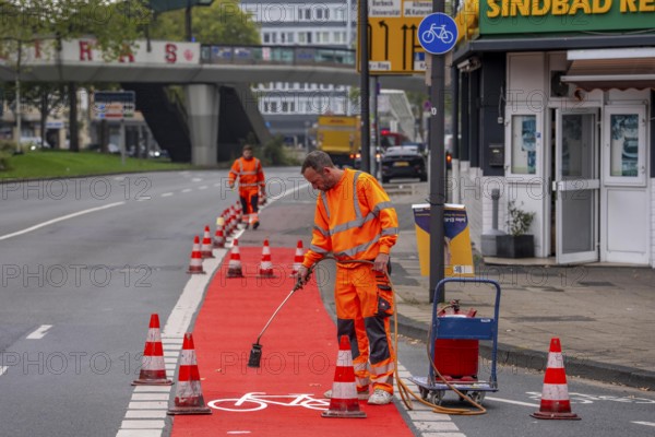 Application of red road surfacing on a cycle lane, inner-city road, so-called cold plastic surfacing, in the colour traffic red, RAL3020, the coloured marking is intended to attract more attention from motorists for cyclists, on cycle paths along roads and at junctions, roundabouts, Essen, North Rhine-Westphalia, Germany