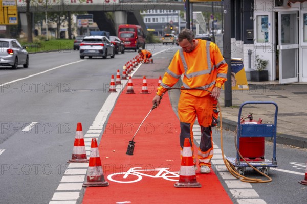 Application of red road surfacing on a cycle lane, inner-city road, so-called cold plastic surfacing, in the colour traffic red, RAL3020, the coloured marking is intended to attract more attention from motorists for cyclists, on cycle paths along roads and at junctions, roundabouts, Essen, North Rhine-Westphalia, Germany