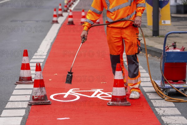 Application of red road surfacing on a cycle lane, inner-city road, so-called cold plastic surfacing, in the colour traffic red, RAL3020, the coloured marking is intended to attract more attention from motorists for cyclists, on cycle paths along roads and at junctions, roundabouts, Essen, North Rhine-Westphalia, Germany
