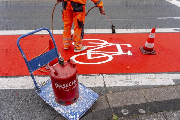 Application of red road surfacing on a cycle lane, inner-city road, so-called cold plastic surfacing, in the colour traffic red, RAL3020, the coloured marking is intended to attract more attention from motorists for cyclists, on cycle paths along roads and at junctions, roundabouts, Essen, North Rhine-Westphalia, Germany