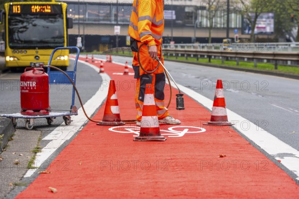Application of red road surfacing on a cycle lane, inner-city road, so-called cold plastic surfacing, in the colour traffic red, RAL3020, the coloured marking is intended to attract more attention from motorists for cyclists, on cycle paths along roads and at junctions, roundabouts, Essen, North Rhine-Westphalia, Germany