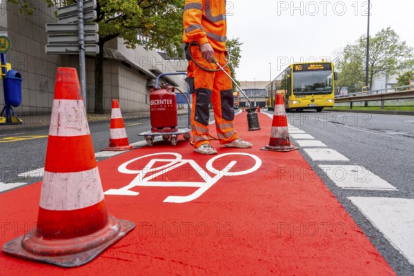 Application of red road surfacing on a cycle lane, inner-city road, so-called cold plastic surfacing, in the colour traffic red, RAL3020, the coloured marking is intended to attract more attention from motorists for cyclists, on cycle paths along roads and at junctions, roundabouts, Essen, North Rhine-Westphalia, Germany