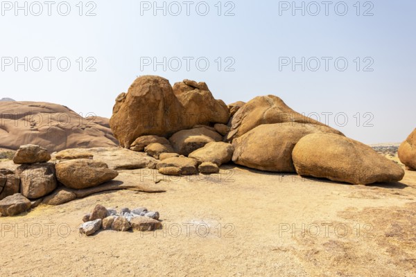 Granite peaks and rugged desert landscape at Spitzkoppe Community Campsite, Namibia. Golden grassland with scattered acacia trees contrasts against dramatic rocky mountains under a clear sky