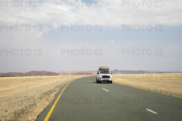 Inside Sossusvlei, gravel roads wind and a car through red dunes to Deadvlei, Big Daddy, and Sesriem Canyon, offering scenic, dusty desert views, Namibia