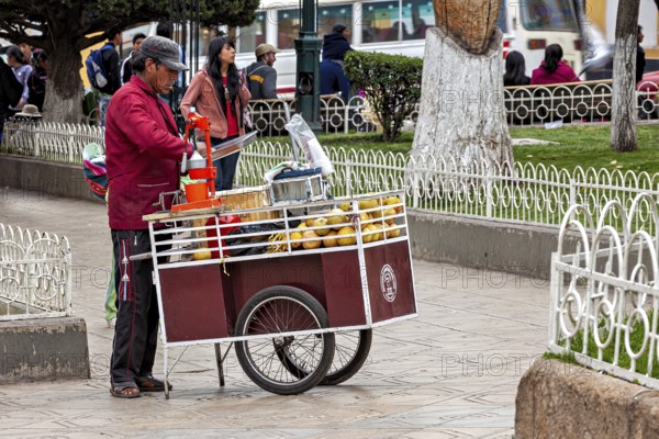 A street vendor operates a fruit stand on a pavement in a busy city, selling fresh juice in the city of Potosi in Bolivia