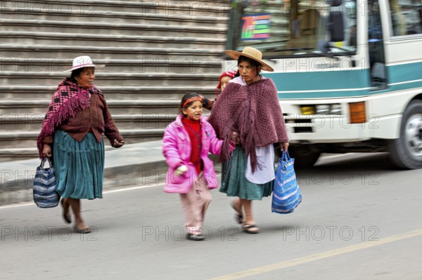 Two woman and a child in traditional dress crossing a street with stairs in the background, woman and people in the streets of Potosi Bolivia