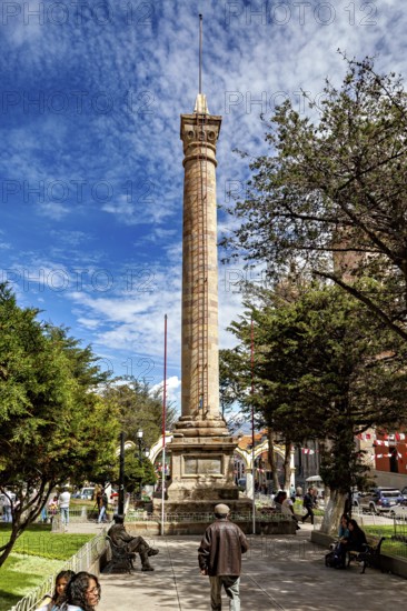 Historical pillar in the park in sunny weather surrounded by trees and people, monument and pillar in the city of Potosi in Bolivia