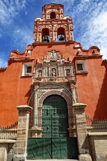 Door of a colonial building with red façade and bell tower under a clear blue sky, The churches of the city of Potosi in Bolivia