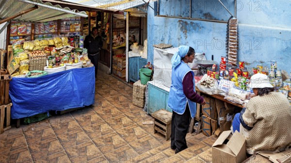 A small shop with two woman behind a table full of food in a traditional setting, market stall selling goods in the market halls of Potosi in Bolivia