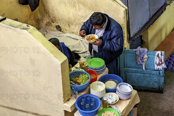 A man eats in a cosy corner with colourful crockery and a laid table, A man eats at a market stall in the market halls of Potosi Bolivia